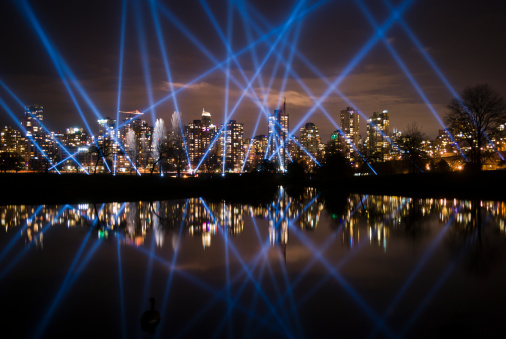 Blue spotlights over Vancouver city reflected in a pond at night.